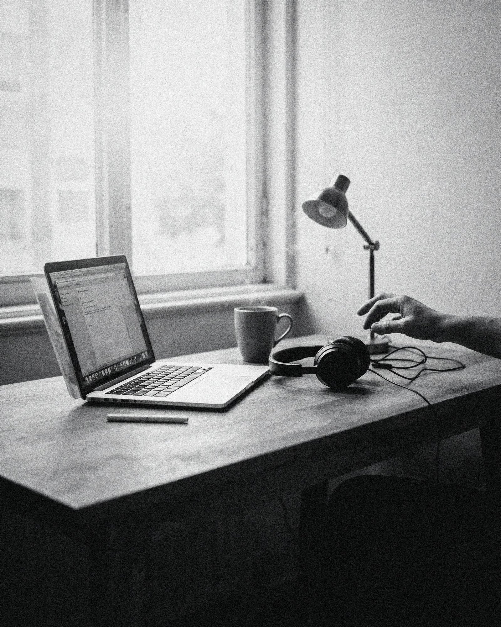 Black and white photo of a small apartment desk with laptop and headphones