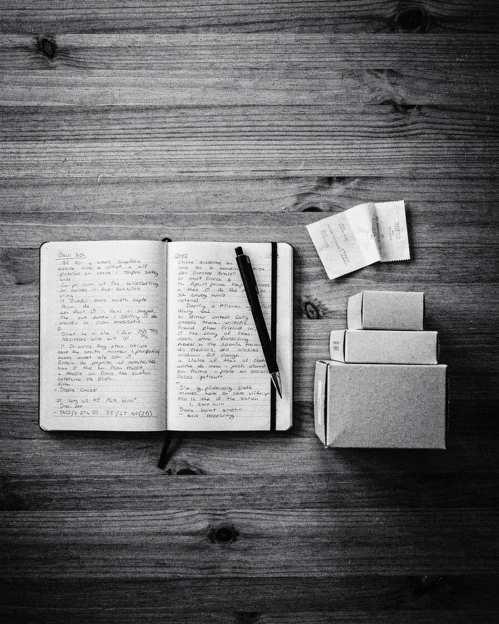 Black and white overhead photo of a notebook, pen and stacked gadget boxes
